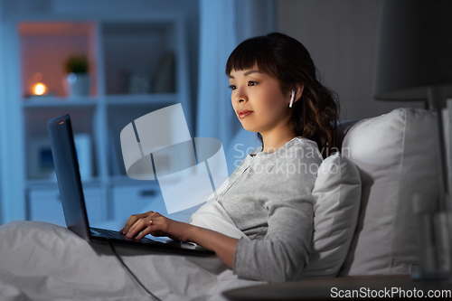 Image of woman with laptop and earphones in bed at night