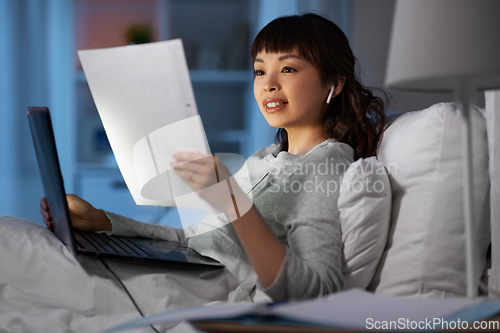 Image of woman with laptop and papers in bed at night