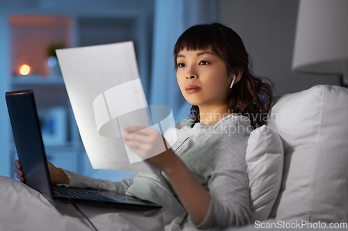 Image of woman with laptop and papers in bed at night