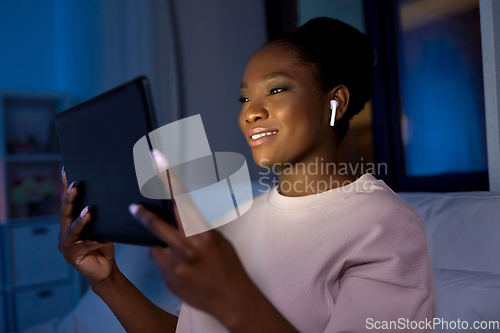 Image of woman with tablet pc in earphones in bed at night