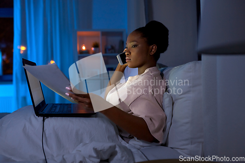 Image of woman with papers calling on phone in bed at night