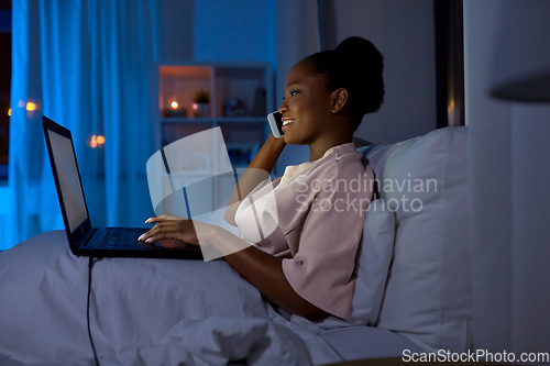 Image of woman with laptop calling on phone in bed at night