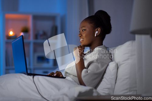 Image of woman with laptop and earphones in bed at night