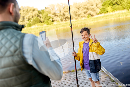 Image of father photographing son with fishing rod on river