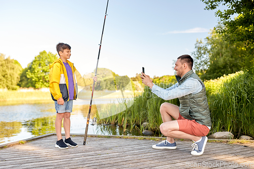 Image of father photographing son with fishing rod on river