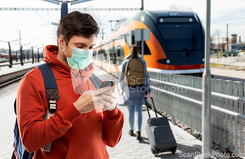 Image of man in mask with smartphone traveling by train