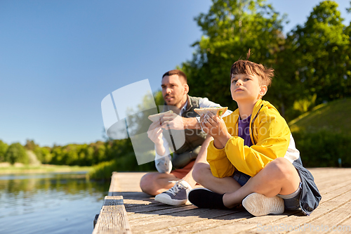 Image of father and son eating sandwiches on river berth