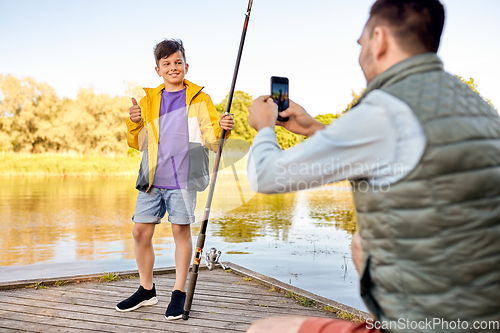 Image of father photographing son with fishing rod on river