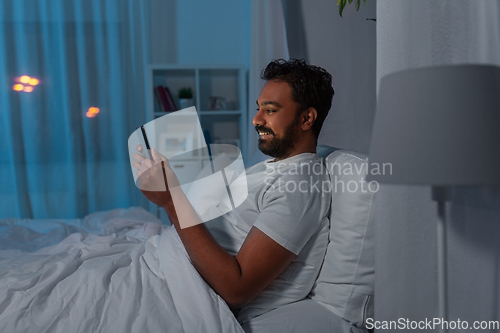 Image of indian man with tablet pc in bed at home at night