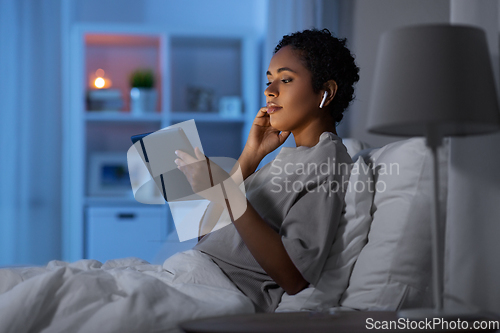 Image of woman with tablet pc in earphones in bed at night