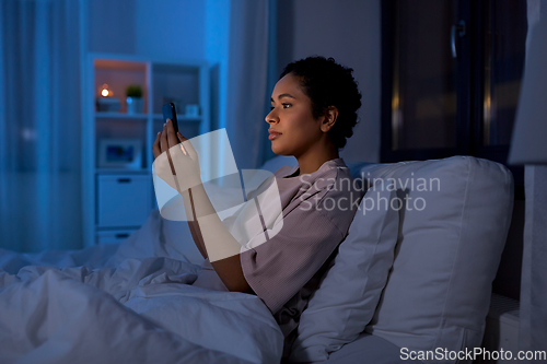 Image of woman with smartphone in bed at home at night