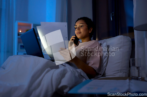 Image of woman with papers calling on phone in bed at night