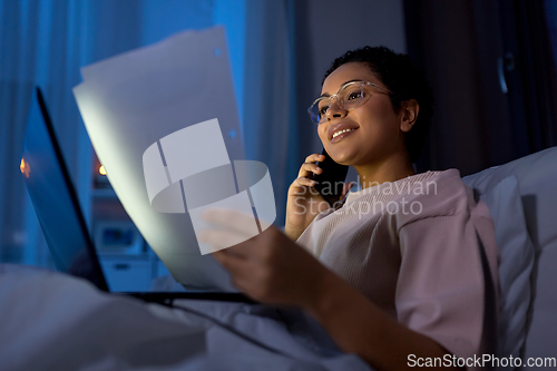 Image of woman with papers calling on phone in bed at night