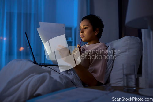 Image of woman with laptop and papers in bed at night