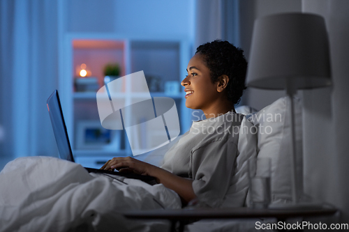 Image of woman with laptop in bed at home at night