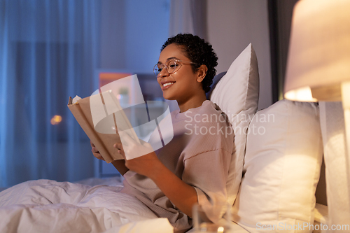 Image of smiling young woman reading book in bed at home