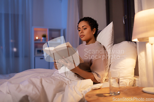 Image of young woman reading book in bed at home