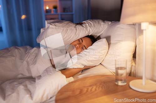 Image of angry african woman lying in bed and closing ears