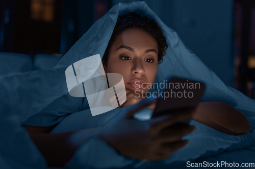 Image of woman with smartphone under duvet in bed at night