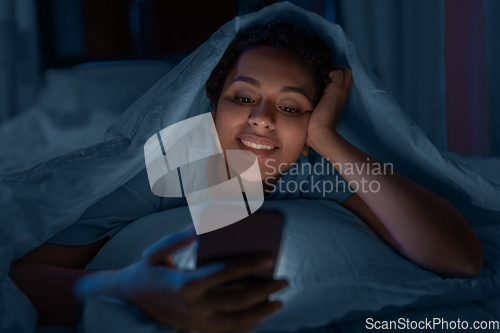 Image of woman with smartphone under duvet in bed at night