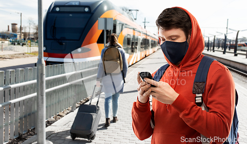 Image of man in mask with smartphone traveling by train