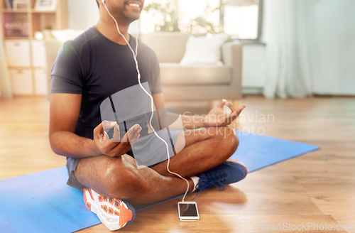 Image of indian man meditating in lotus pose at home