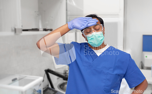 Image of tired indian male doctor in blue uniform and mask