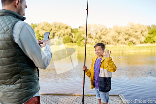 Image of father photographing son with fishing rod on river