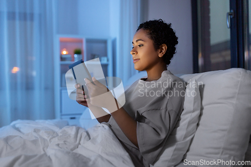 Image of woman with tablet pc in bed at home at night