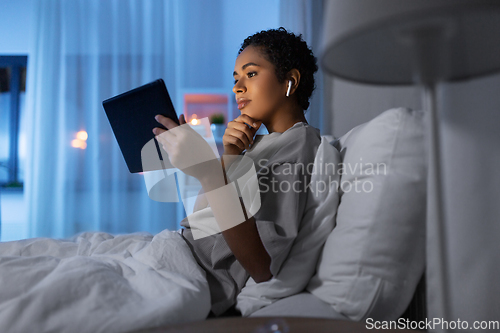 Image of woman with tablet pc in earphones in bed at night