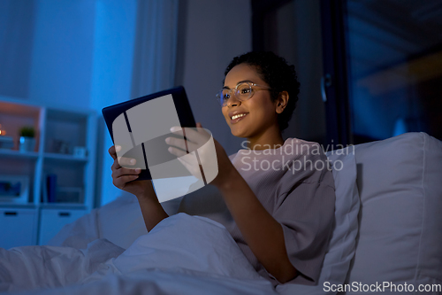 Image of woman with tablet pc in bed at home at night