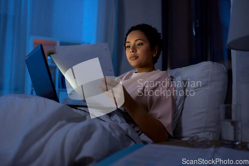 Image of woman with laptop and papers in bed at night