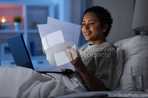 Image of woman with laptop and papers in bed at night