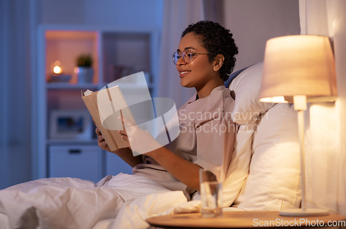 Image of smiling young woman reading book in bed at home