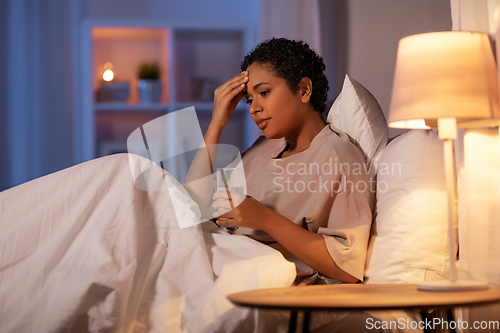 Image of stressed african woman lying in bed at night