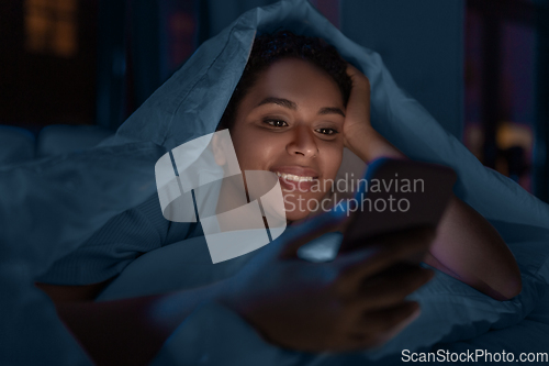 Image of woman with smartphone under duvet in bed at night