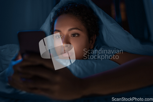 Image of woman with smartphone under duvet in bed at night