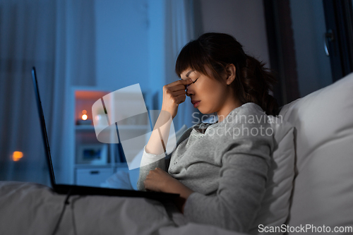 Image of stressed woman with laptop working in bed at night