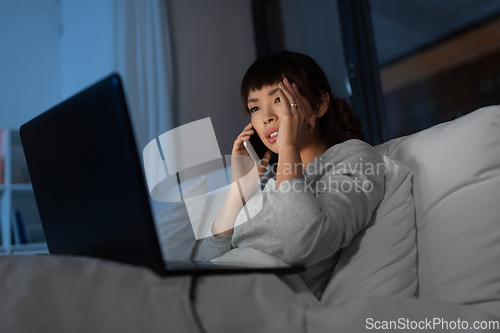 Image of woman with laptop calling on phone in bed at night