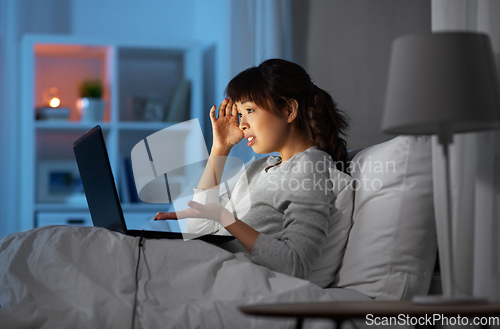 Image of stressed woman with laptop working in bed at night