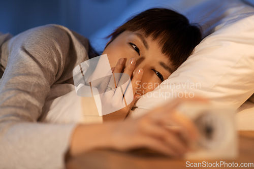 Image of asian woman with clock yawning in bed at night