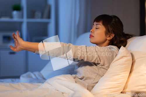 Image of tired asian woman stretching in bed at night