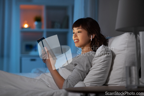 Image of woman with tablet pc in earphones in bed at night