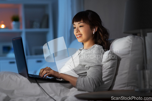 Image of woman with laptop and earphones in bed at night