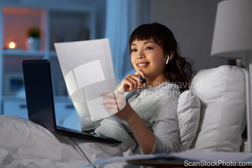 Image of woman with laptop and papers in bed at night