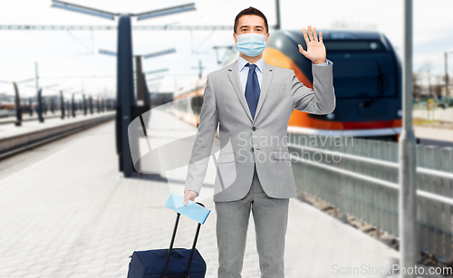 Image of businessman in mask with travel bag over train