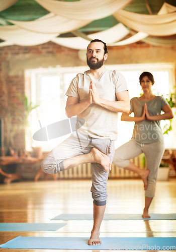 Image of man and woman doing yoga tree pose at studio