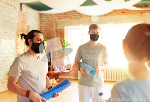 Image of group of people in masks with mats at yoga studio