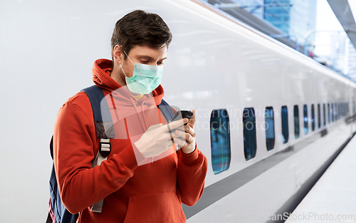 Image of man in mask with smartphone traveling by train