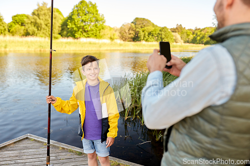 Image of father photographing son with fishing rod on river